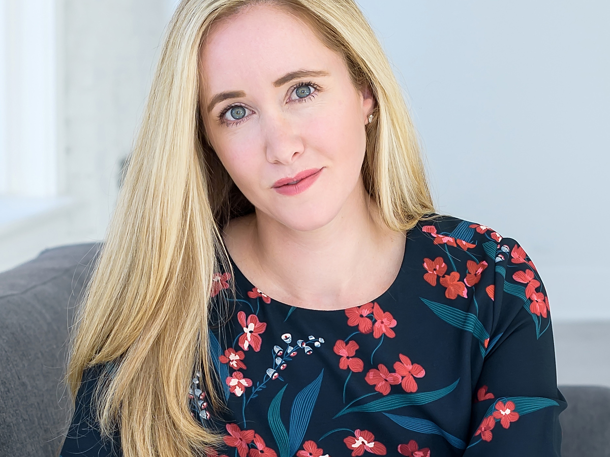 Headshot of Rachel Loftspring. She is sitting on a couch and wearing a floral pattern dress.