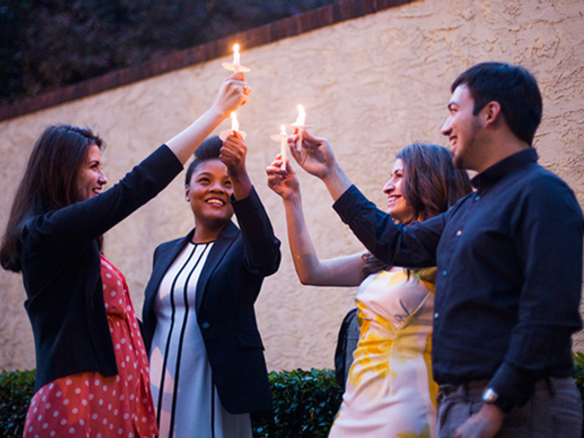 A diverse group of students standing together holding lit candles together in the air.