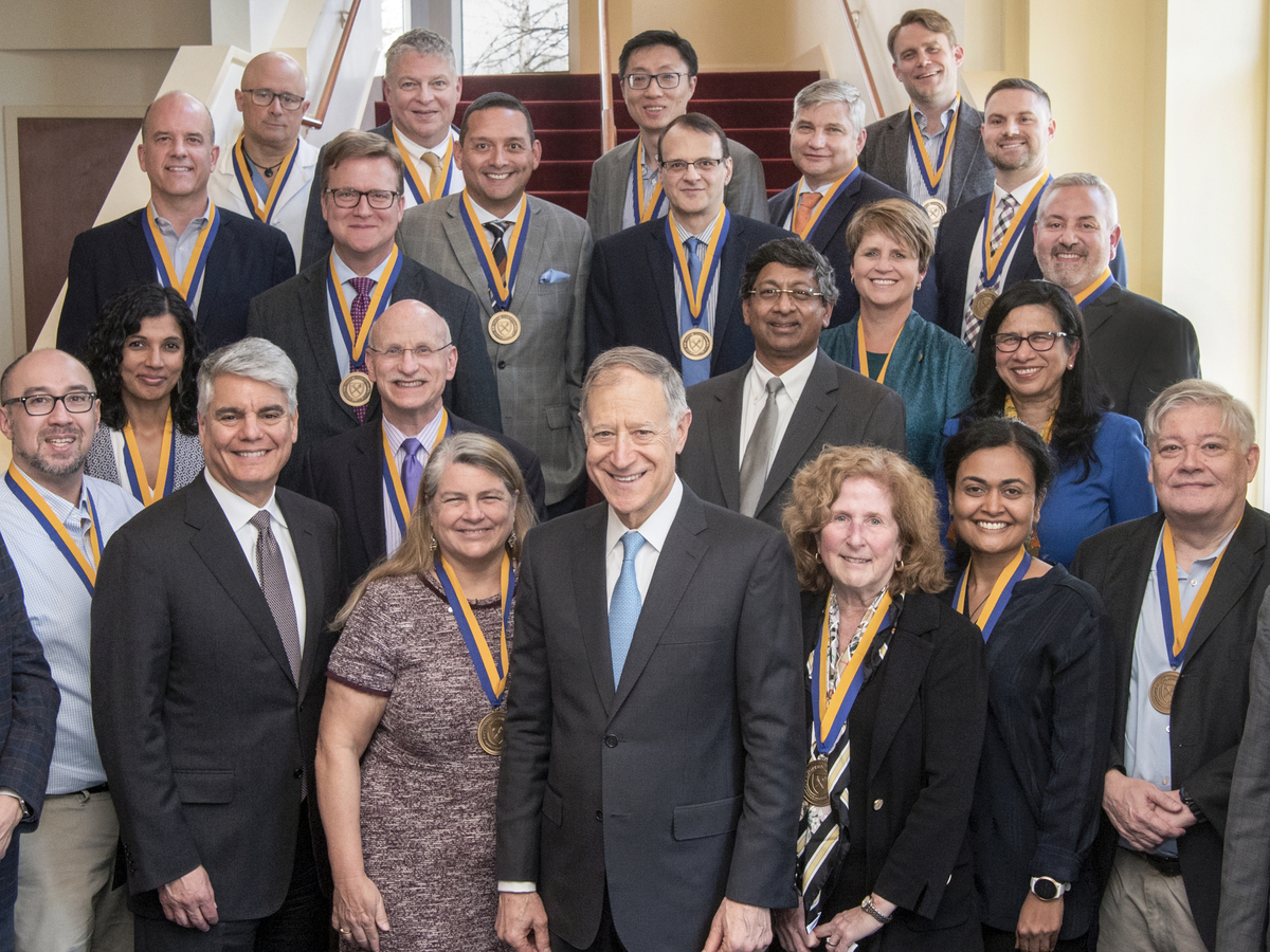 A diverse group of faculty standing together in on a set of stairs with medals hanging from their necks.