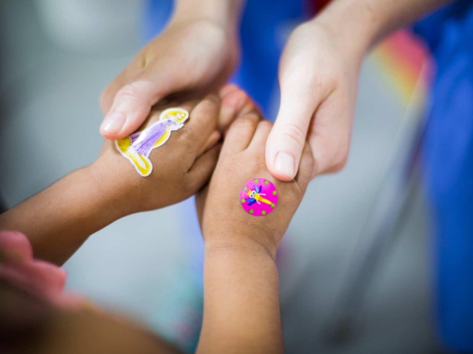 Nursing holding a child's hands with colorful stickers atop the child's hands